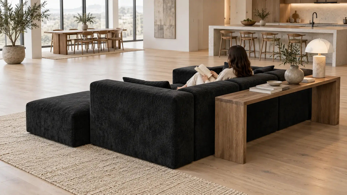 Black MONVANE L-Shaped Modular Couch floated in the middle of an open-plan room with a narrow console table behind it (AI-generated illustration, not a customer photo)
