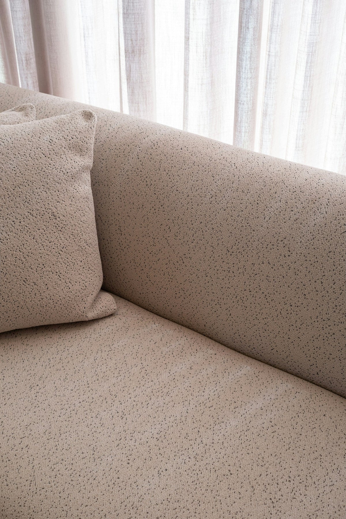 Nubby beige upholstery across a sofa seat, pillow and curved arm.