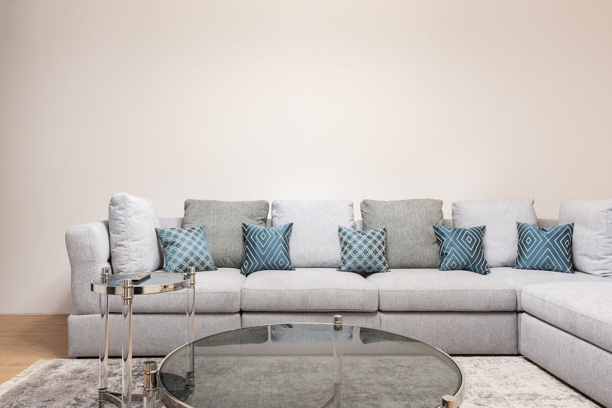 Gray corner sofa with patterned cushions and a round glass coffee table in front.