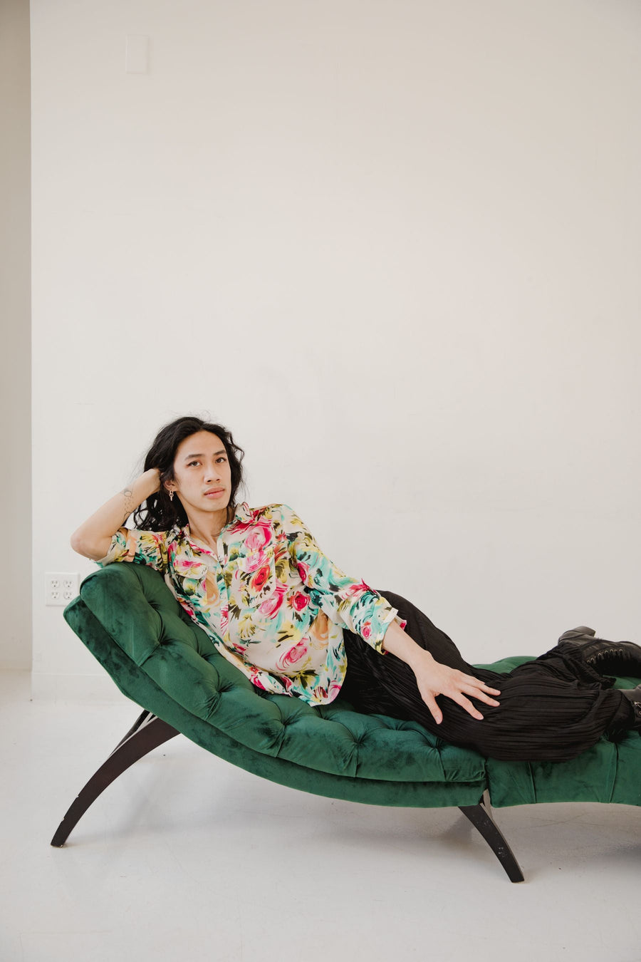 A person reclining on a green tufted chaise with a curved upholstered back and extended seat.