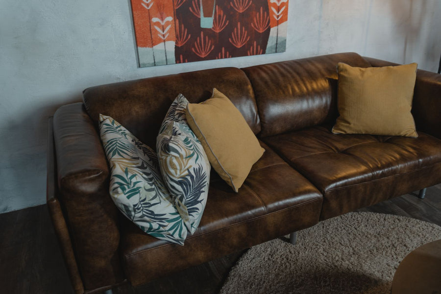 Dark brown leather sofa with mustard and pale leaf-patterned pillows against a light blue-gray wall.