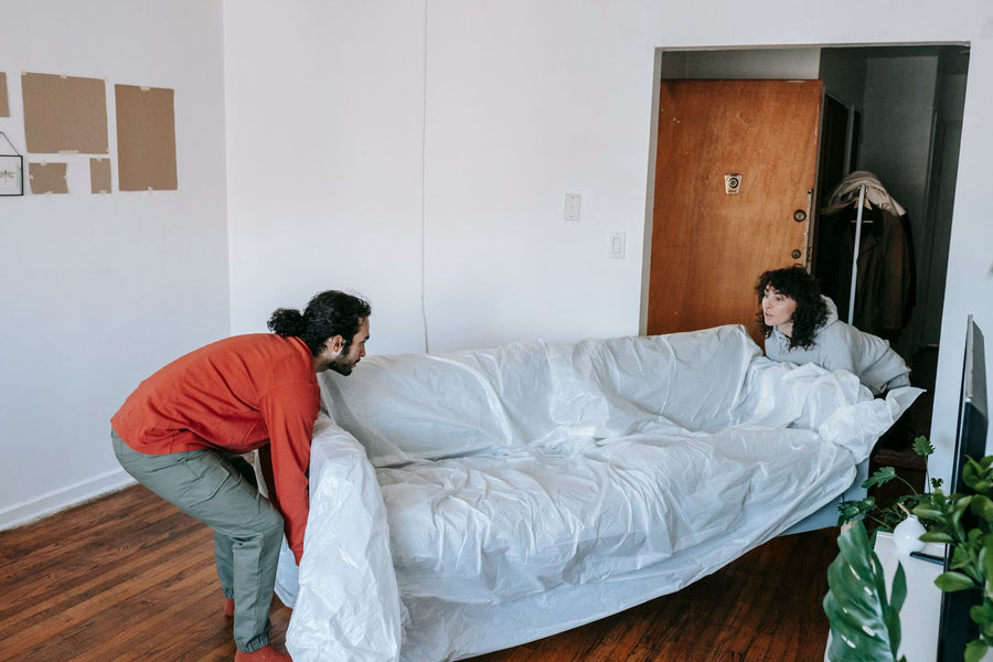 Two adults lifting a sofa wrapped in white protective material.