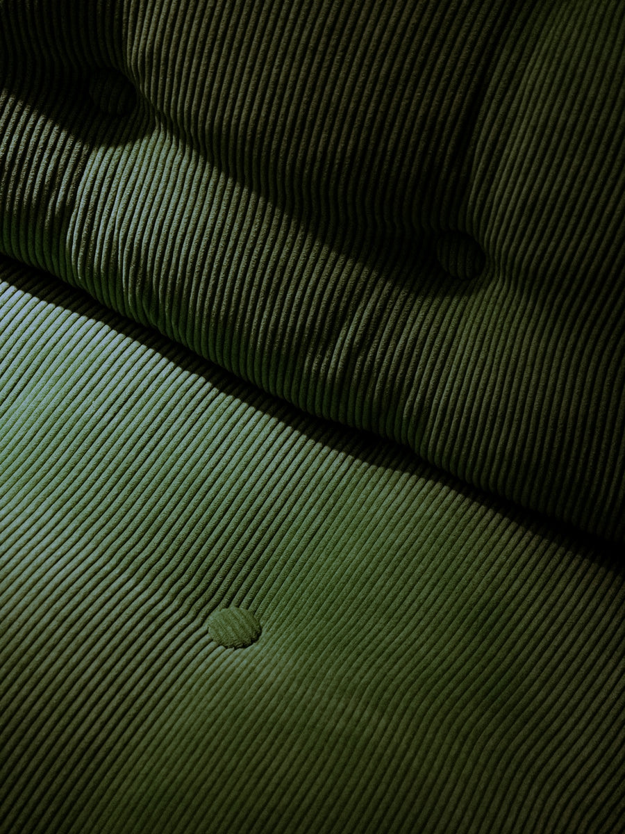 Raised green corduroy ribs across a button-tufted sofa seat and back