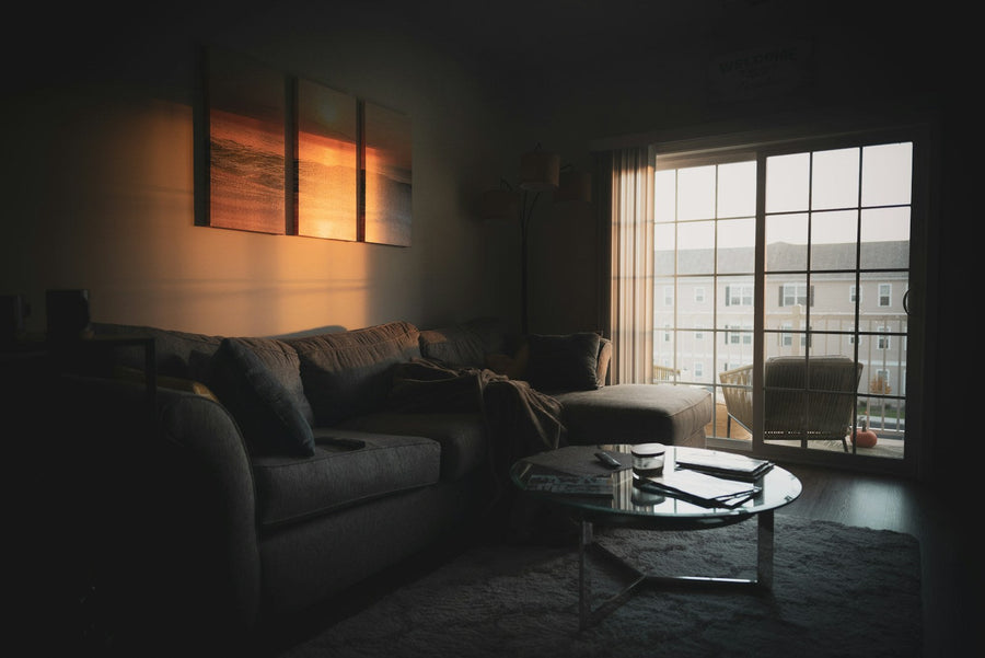 A gray chaise sofa and round glass table beside sliding balcony doors