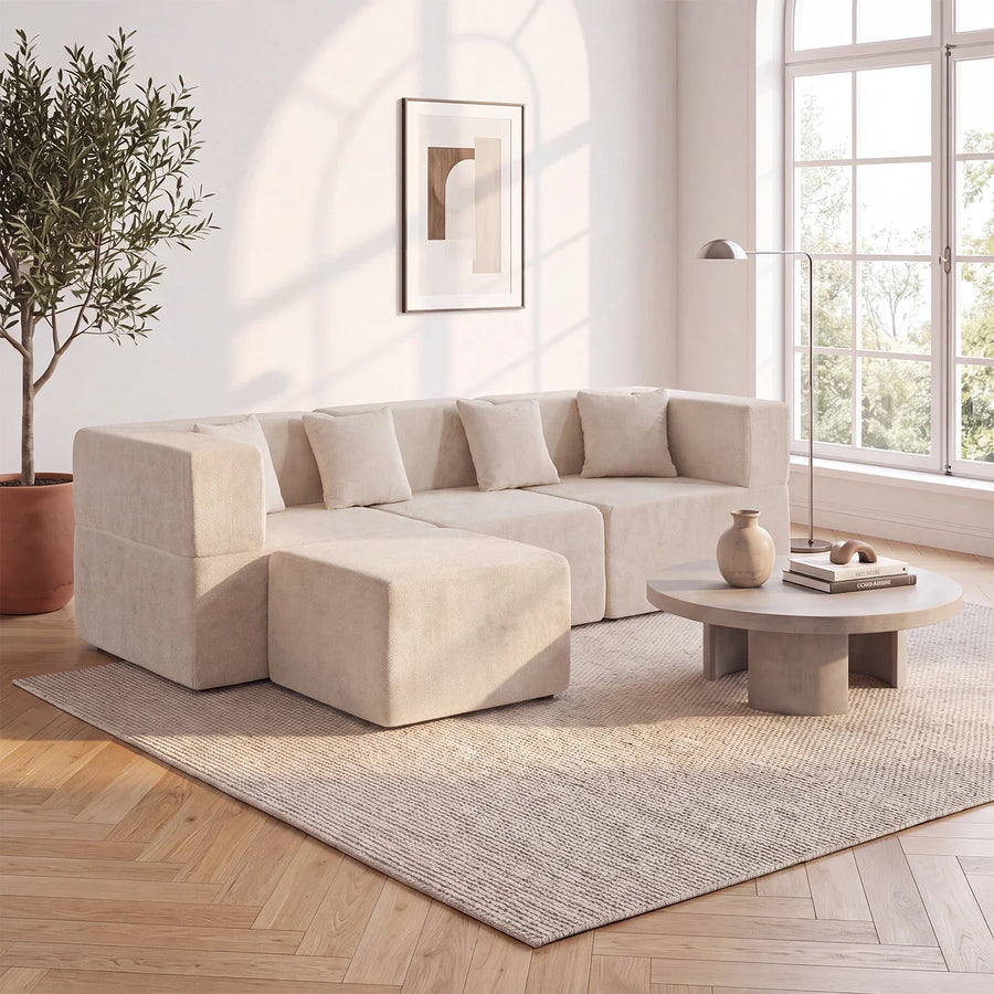 Beige L-shaped modular sofa with loose back pillows and a separate ottoman in a bright living room