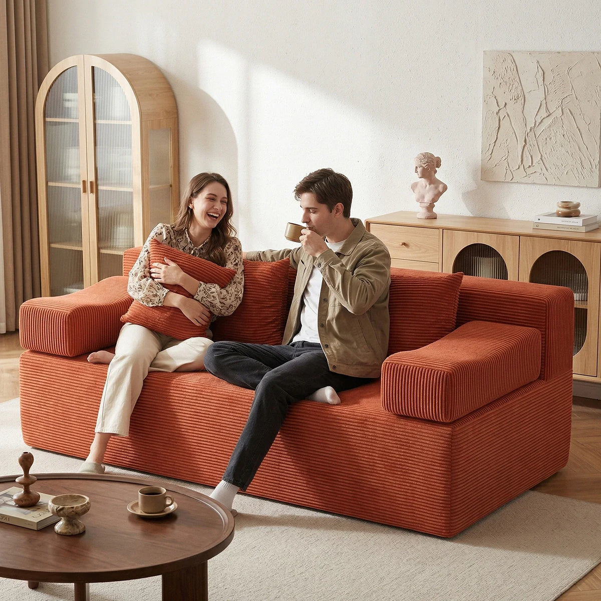 Two adults sharing a red corduroy loveseat in a compact living room