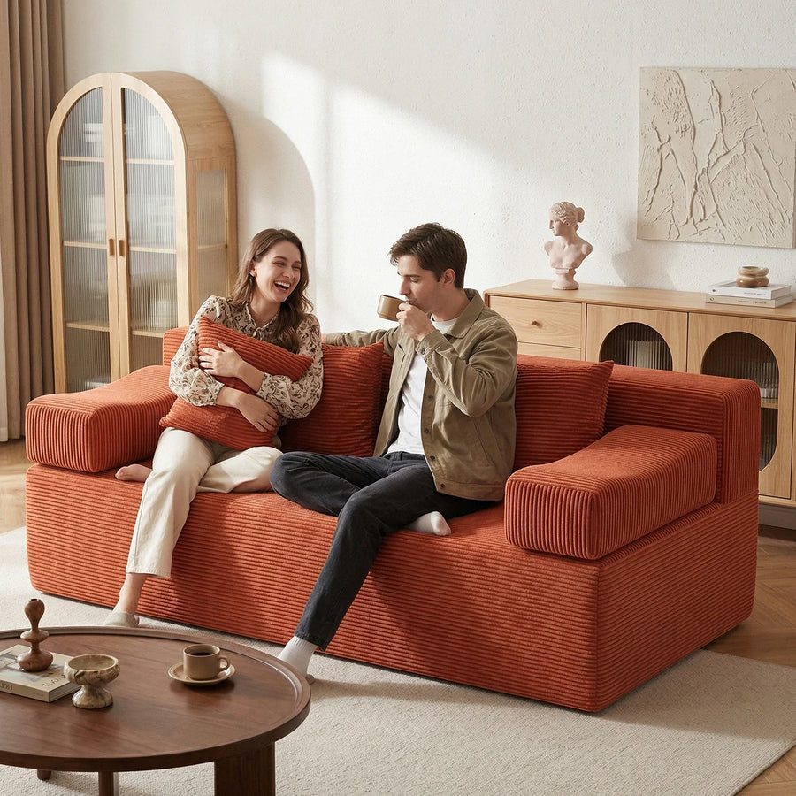 Two adults sharing a red corduroy loveseat in a compact living room