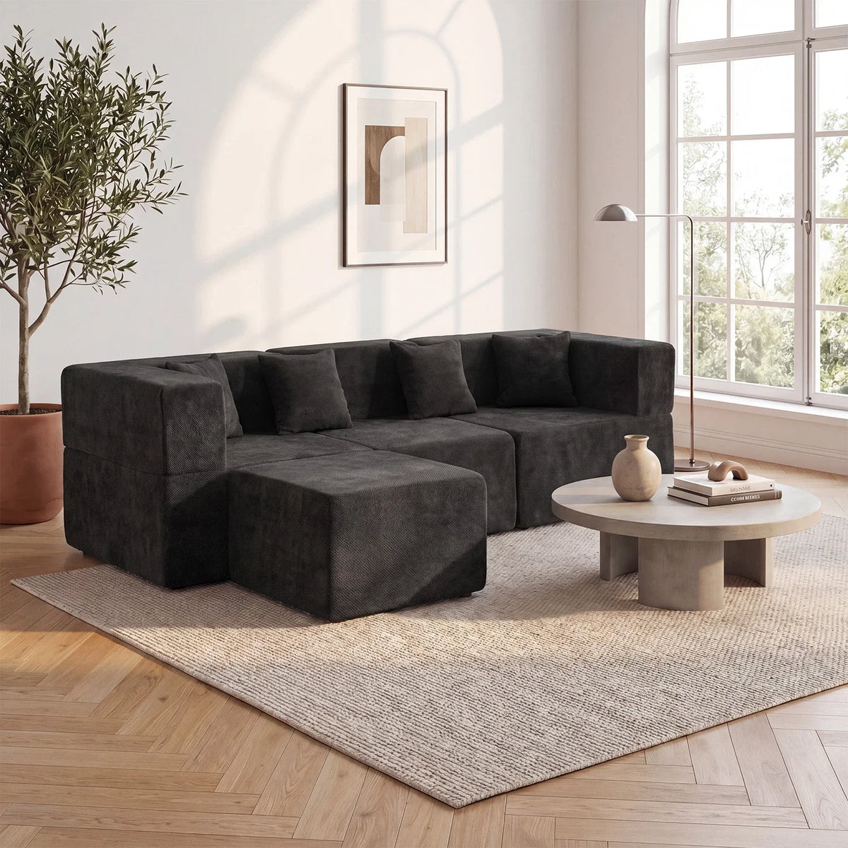 Black L-shaped sofa on a light rug in a bright living room with warm wood flooring.