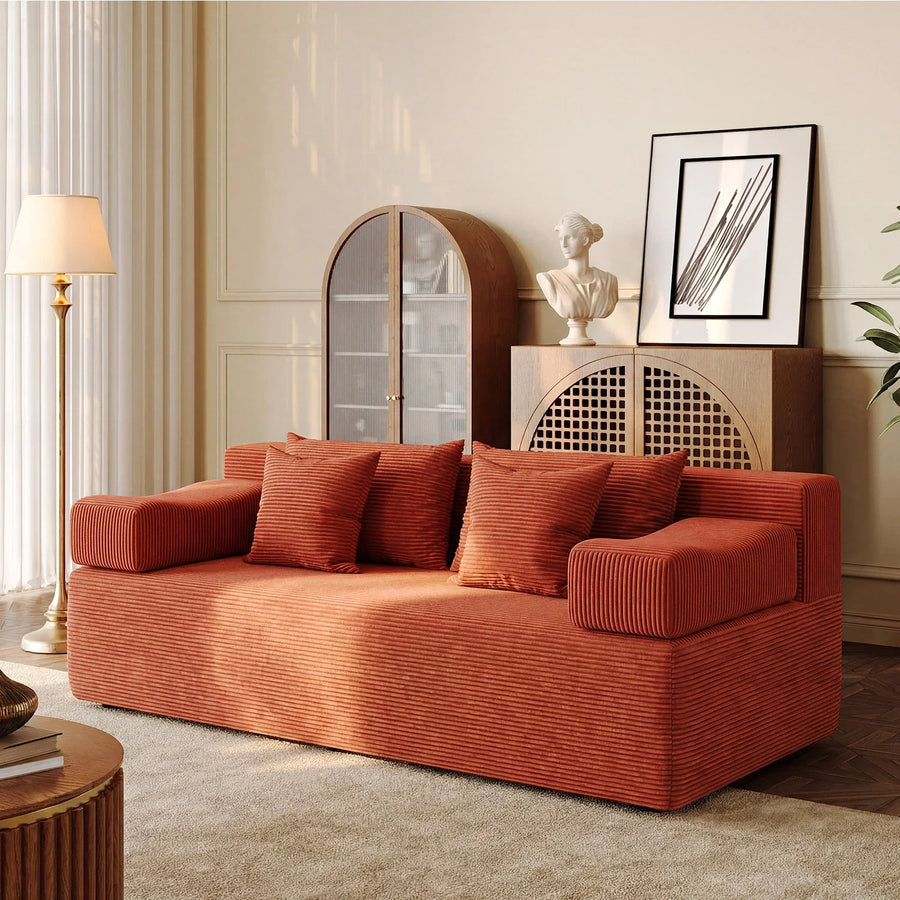 Warm rust corduroy Monvane loveseat styled with four matching square cushions in a pale room with warm wood.