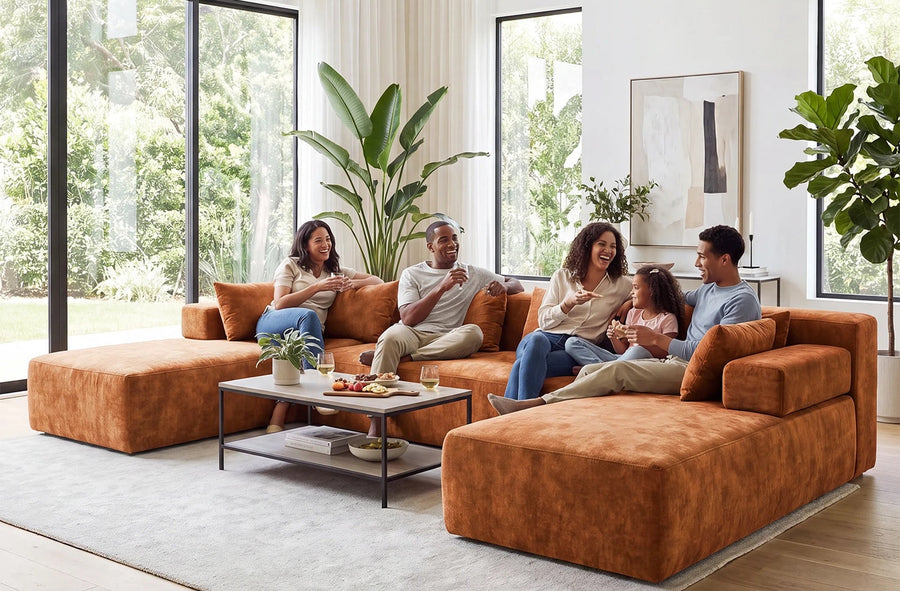 Five people seated on an orange U-shaped Monvane sectional around a coffee table in a bright living room.