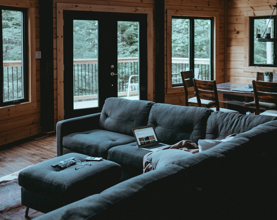 Gray L-shaped sectional with a separate upholstered ottoman in front in a wood-paneled living room.