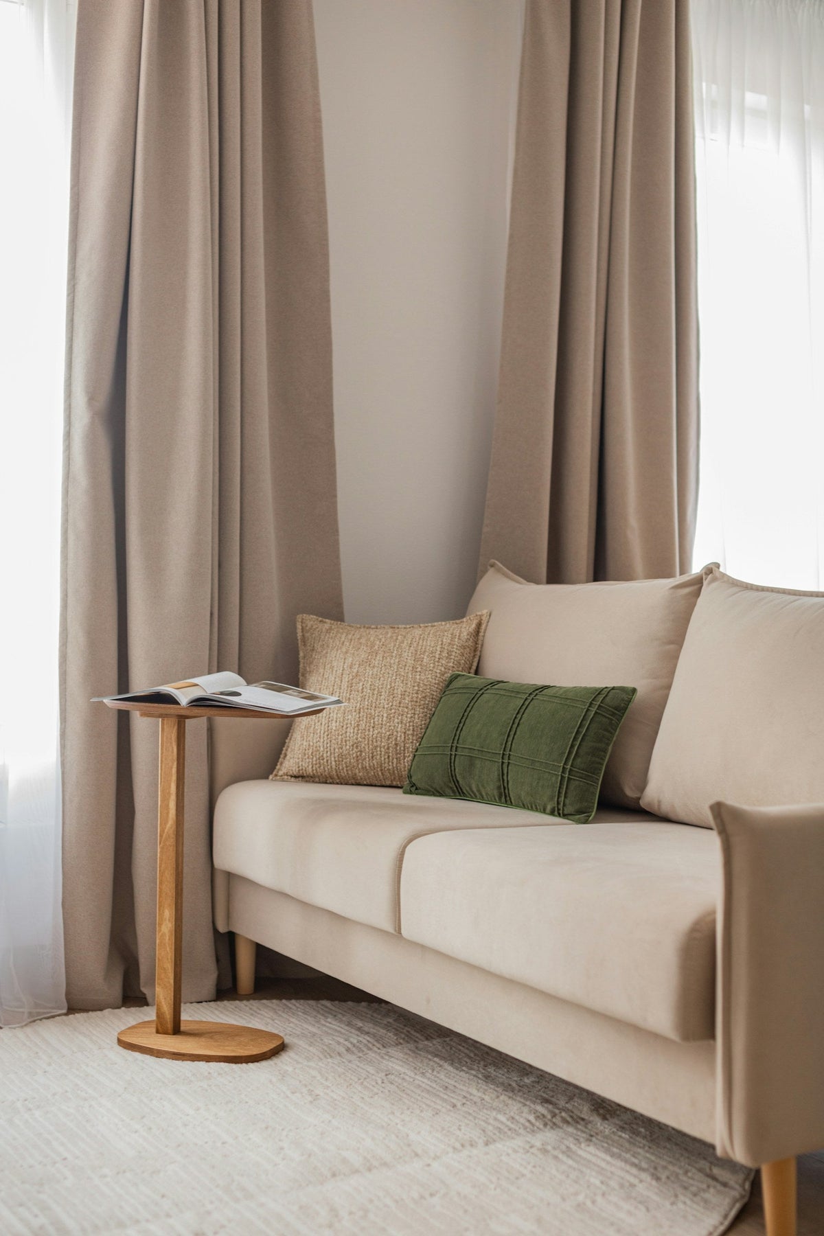 Beige sofa with two small decorative pillows in front of large back cushions and a slim side table.