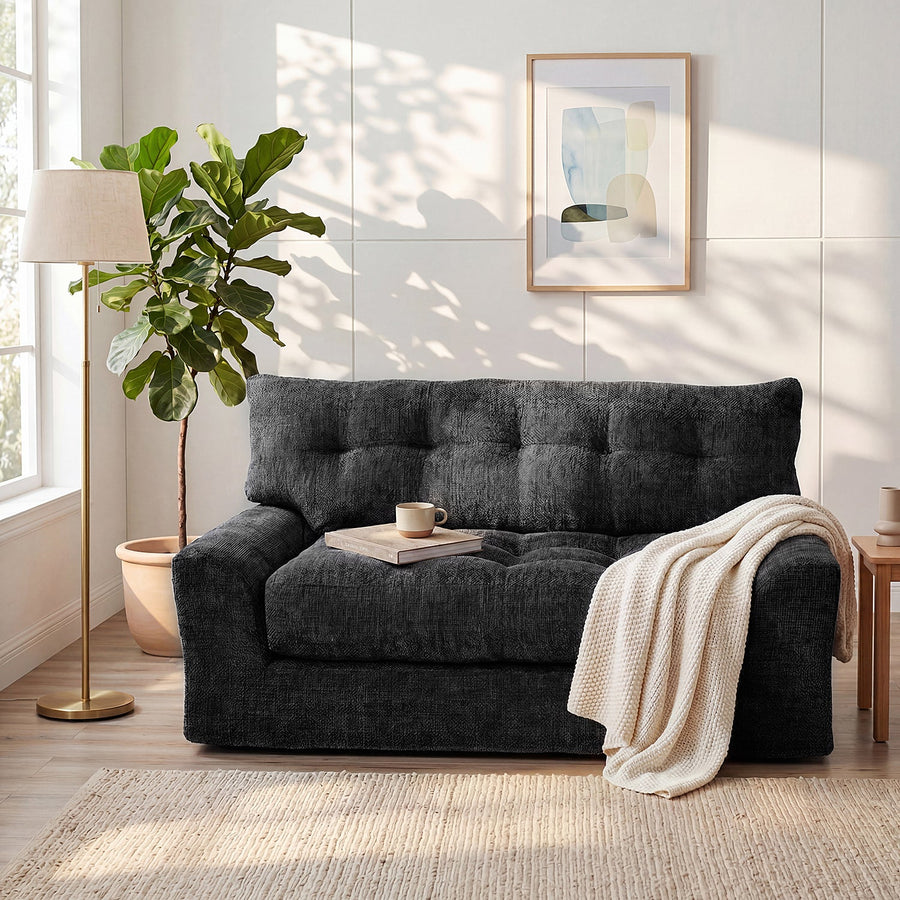 Black Monvane Convertible Loveseat with a tufted back, wide arms, book, cup and draped blanket.
